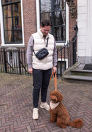 Personne portant la pochette noire cuir à l'épaule et promenant un labradoodle marron en laisse