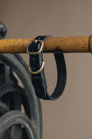 Collier pour chien en cuir noir accroché sur une barre en bois