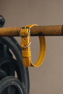 Collier pour chien en cuir moutarde accroché sur une barre en bois