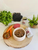 Pâtée pour chien dans une gamelle blanche avec la boîte, des légumes et un steak à coté